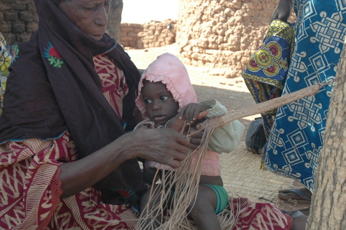 Fulani lady weaving a horses girth strap with a child on her lap